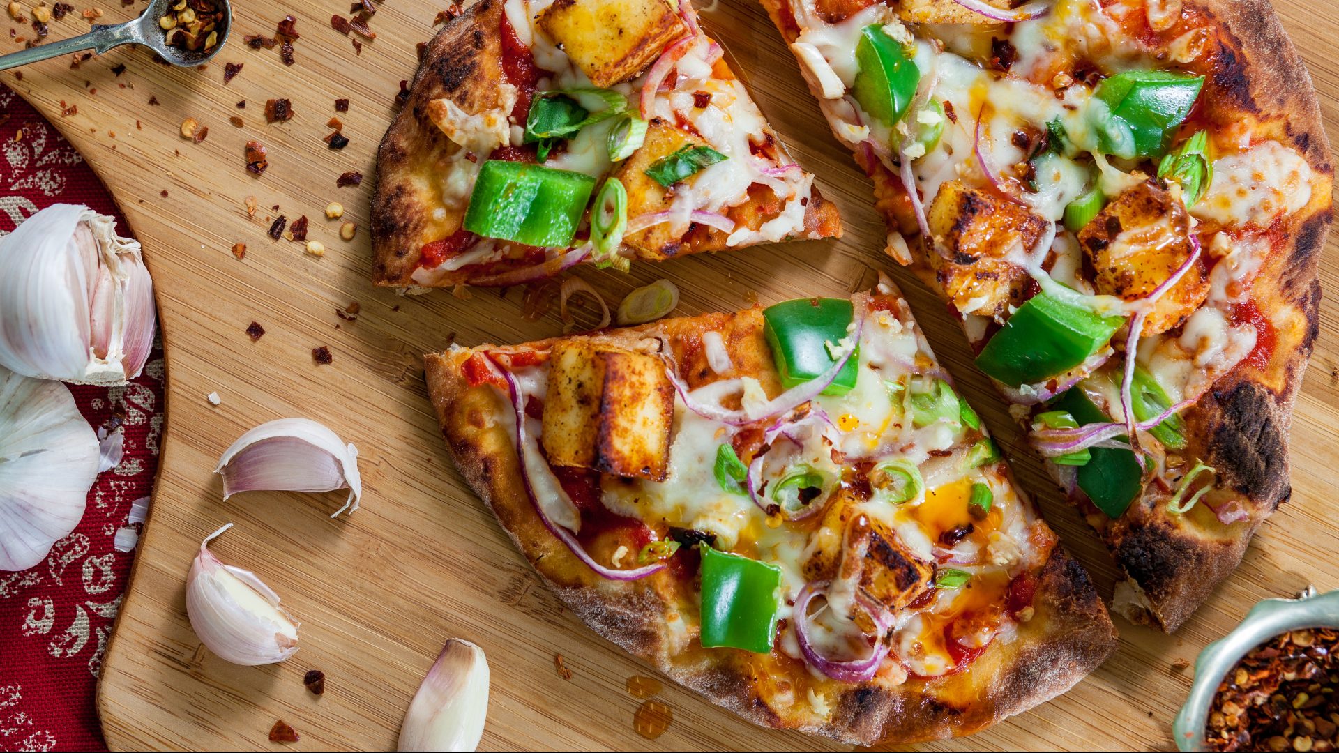 Stonefire Naan as an onion and pepper pizza. High-quality pizza crusts for foodservice with garnishes surrounding a restaurant menu inspired setting